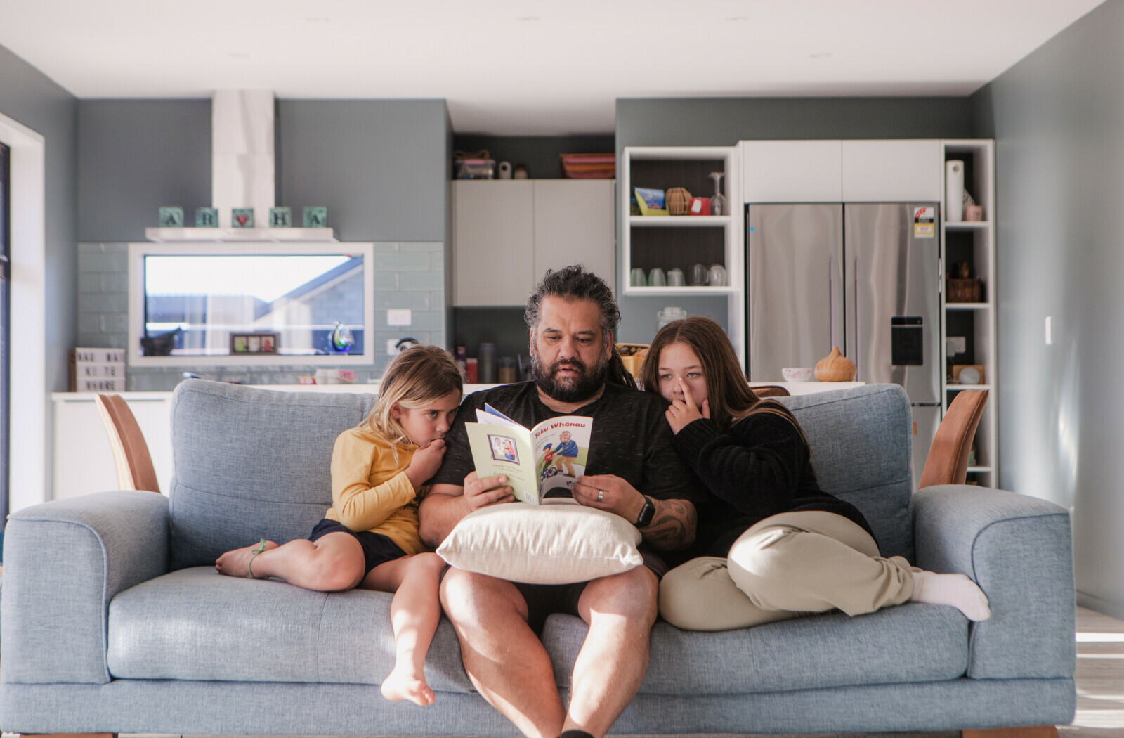 Māori father reads a te reo children's book to his two kids.
